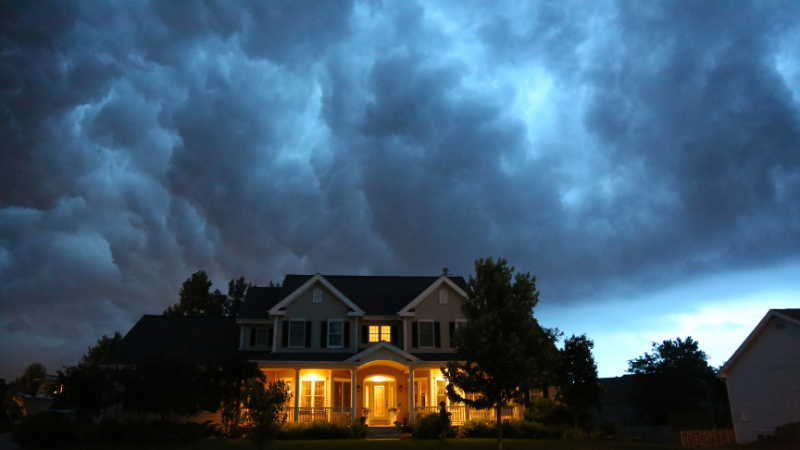 house with lights on and stormy skies